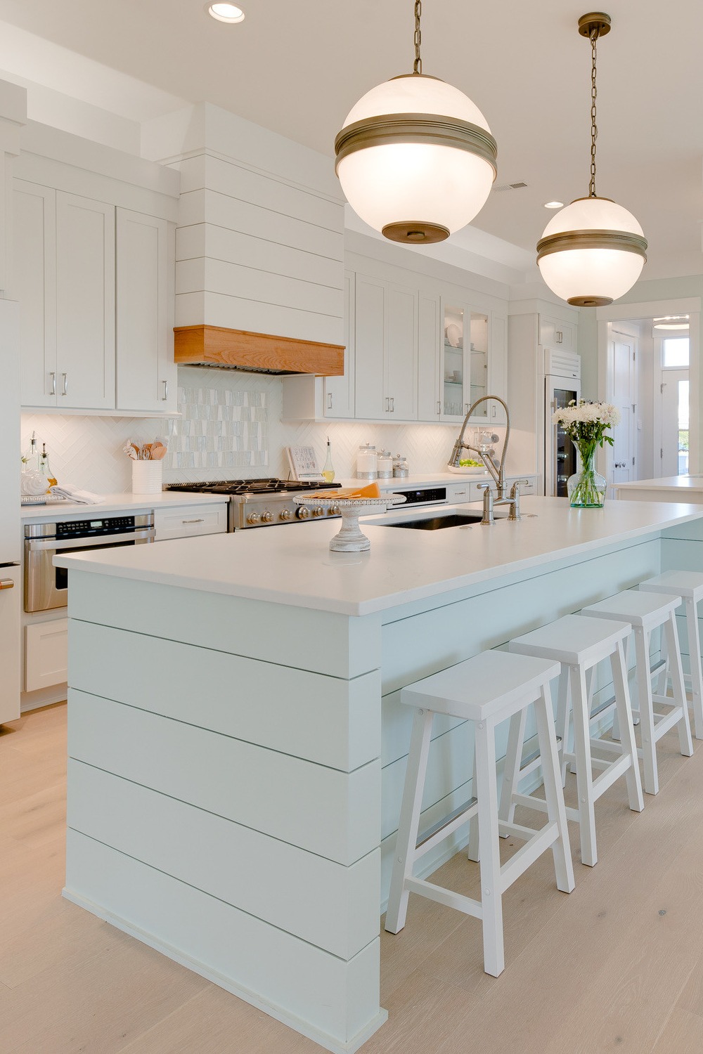 White Glass Tile Backsplash White Appliances Light Hardwood Flooring Quartz Counters Cabinetry Pendant Lights