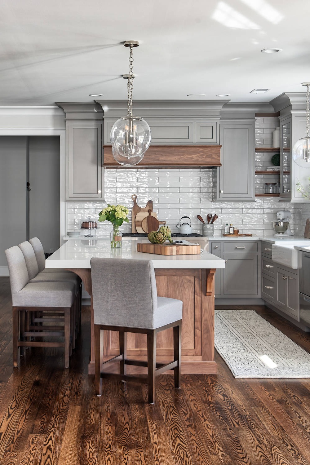 Grey Cabinetry Quartz Counters Subway Tiles Brown hardwood Flooring Farmhouse Sink Pendant Lights