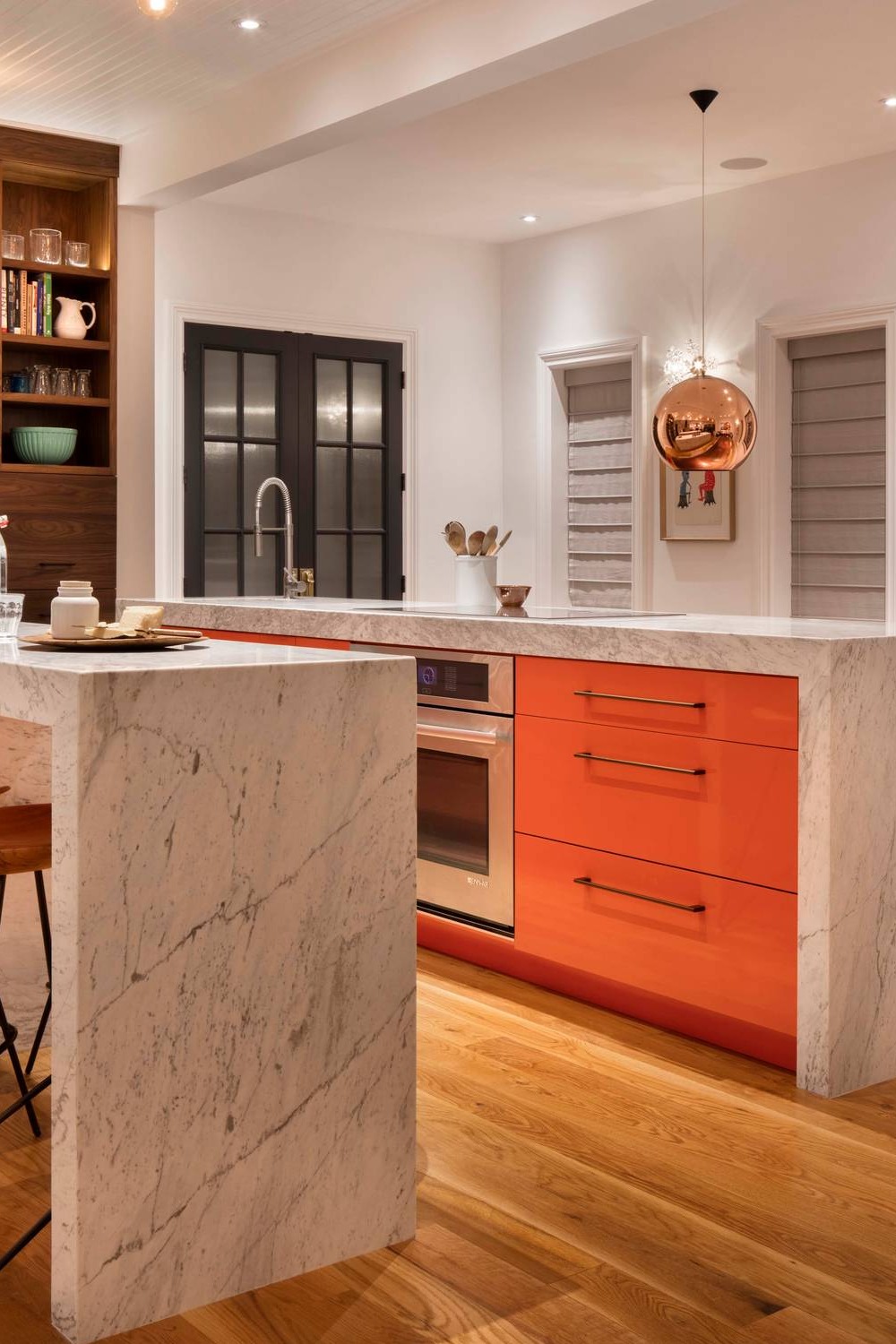 White Carrara Marble Waterfall Countertop Orange Cabinetry Hardwood Flooring Copper Pendant Lights